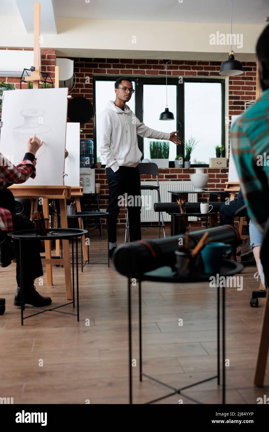 Les étudiants de peintre qui créent des dessins sur toile à l'aide d'un crayon graphique lors d'un cours d'art en studio créatif. Équipe multiethnique dessin vase modèle sur toile travaillant à la technique créative. Banque D'Images