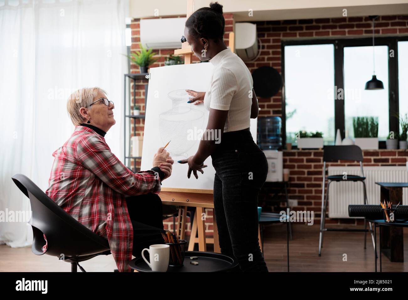 Jeune professeur d'art expliquant la technique d'esquisse à un étudiant senior pendant le cours de créativité. Artiste femme dessin vase modèle sur toile blanche à l'aide d'un crayon graphique. Résolutions du nouvel an Banque D'Images