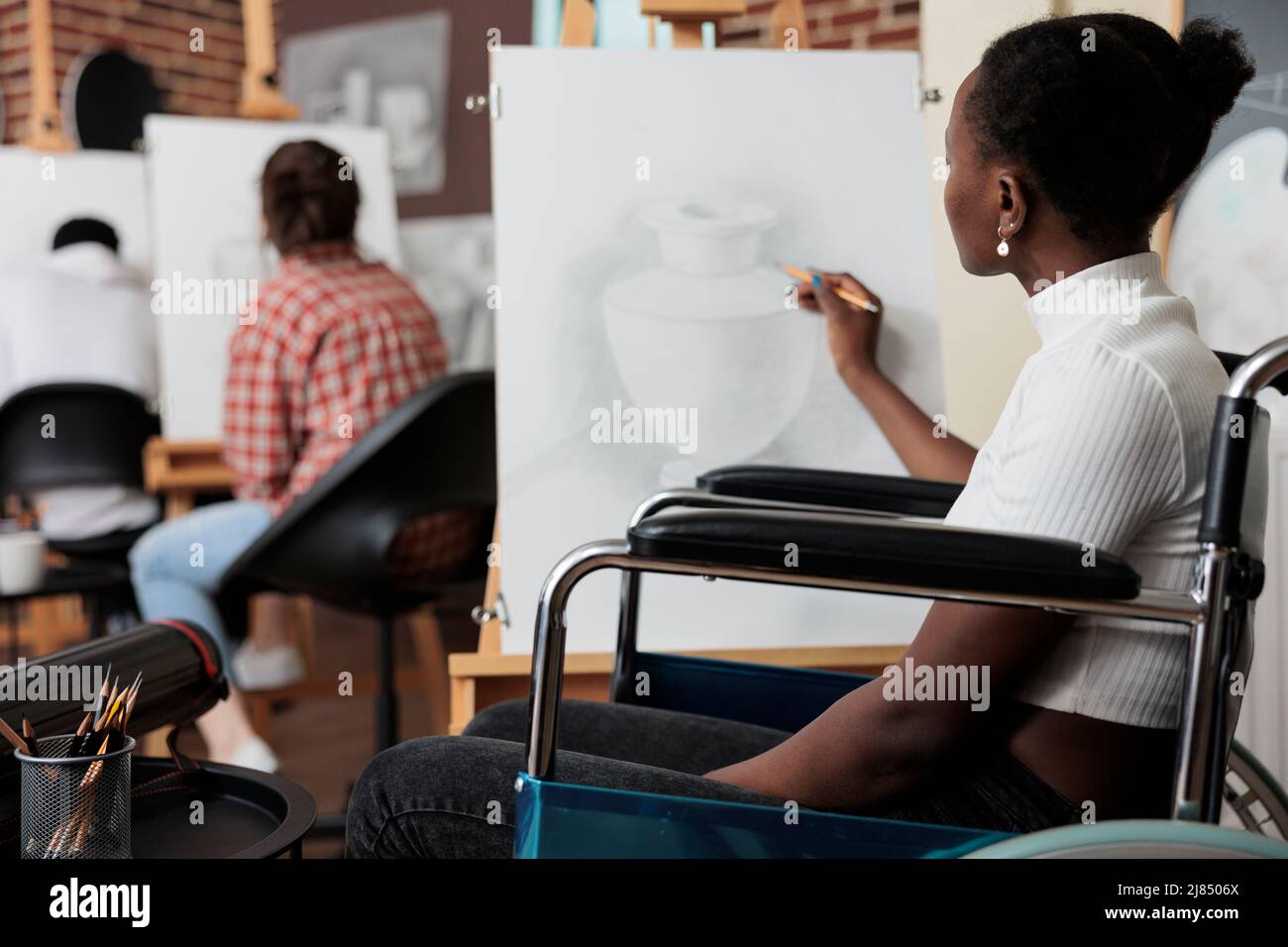 Étudiant paralysé en fauteuil roulant en train de s'adapter au cours  artistique dessin vase croquis sur toile à l'aide d'un crayon graphique  travaillant à la technique d'esquisse. Équipe diversifiée développant des  compétences