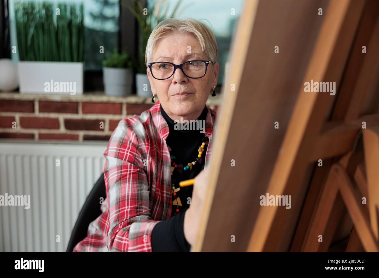Portrait de la vieille artiste femme dessinant un croquis sur toile graphique pendant les cours d'art dans un lieu de travail mural en brique. Groupe de personnes apprenant à dessiner à l'aide de la technique d'illustration. Résolutions du nouvel an Banque D'Images