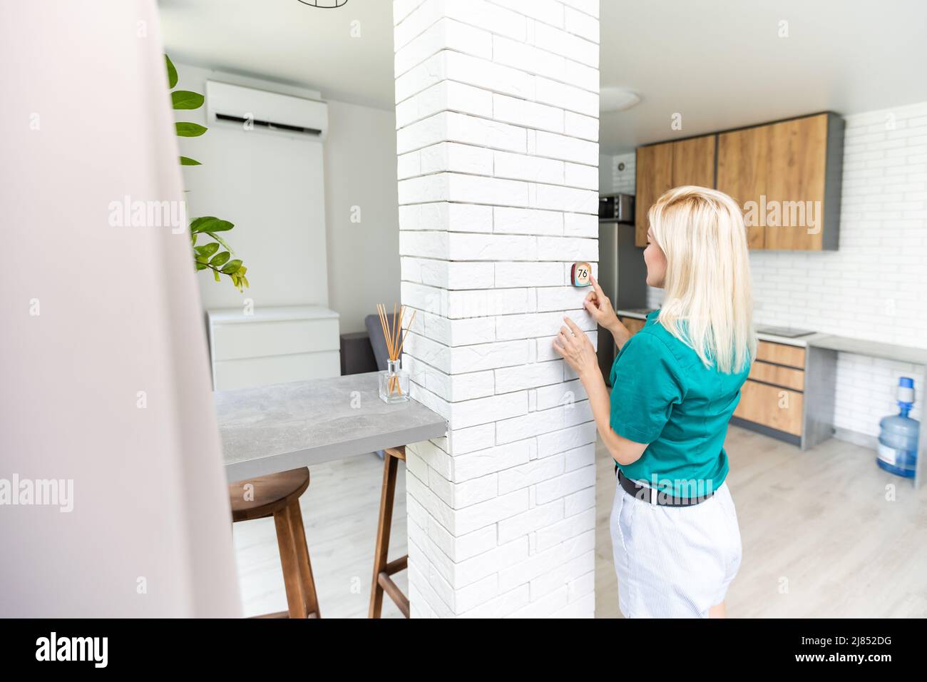 Une femme appuie sur le bouton fléché vers le haut d'un thermostat d'intérieur fixé au mur avec affichage numérique indiquant la température. Une image de concept pour l'électricité Banque D'Images