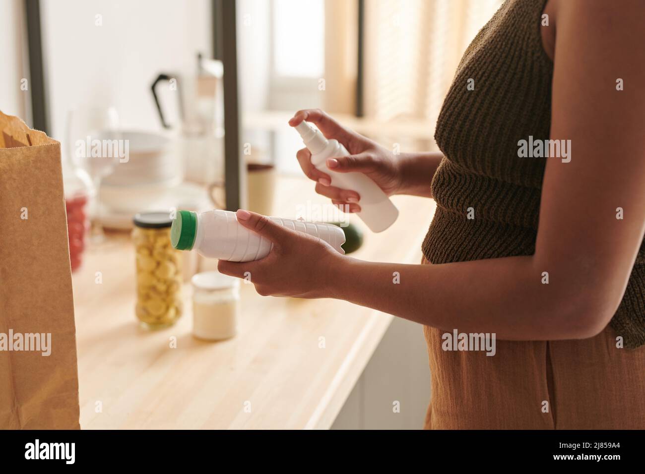 Gros plan de l'emballage alimentaire noir non reconnaissable de femme désinfectante avec assainisseur dans la cuisine, règles de protection contre les coronavirus Banque D'Images