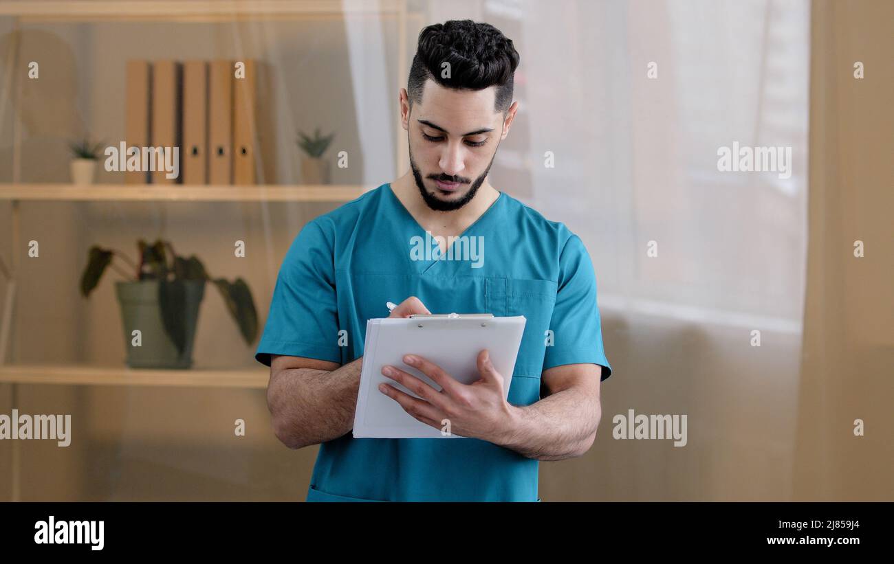 Hispanique médecin homme médecin homme thérapeute médical porter uniforme debout dans la clinique de l'hôpital écrire des notes remplir le formulaire médical avis d'assurance détaillé Banque D'Images