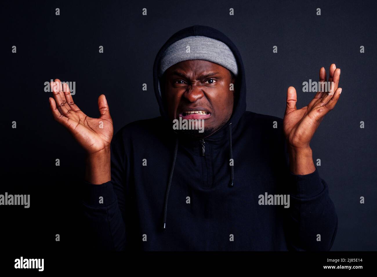 inquiet jeune afro-américain mele portant un chapeau gris et un sweat à capuche noir se cachant du studio de l'attaquant du violeur, le sol noir Banque D'Images