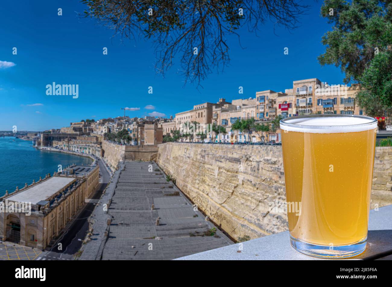 Verre de bière légère avec vue sur le mur de la ville et le port de la Valette, Malte. Banque D'Images