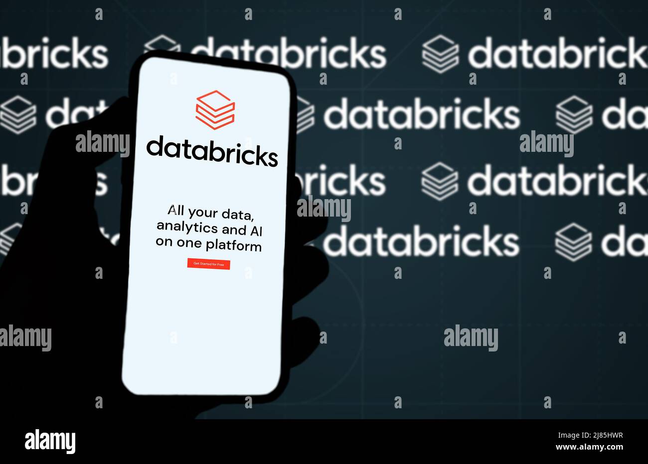 San Francisco, CA, US, mai 2022 : main tenant un téléphone avec la page Web de la compagnie Databricks à l'écran. En arrière-plan le logo Databricks flou et répétition Banque D'Images