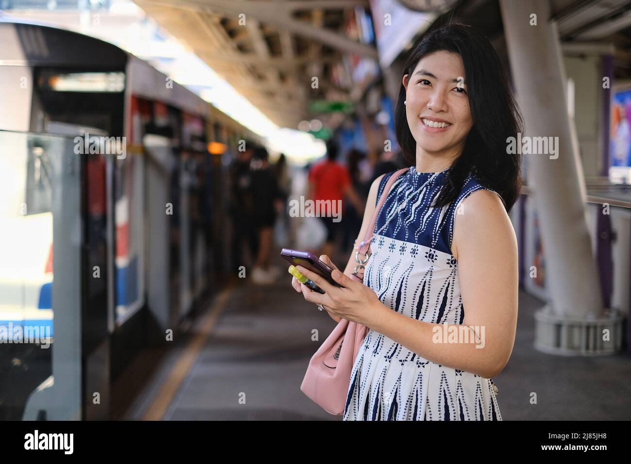 Une jeune femme d'affaires asiatique confiante et attrayante utilise son téléphone portable tout en attendant que son train se trouve à une gare pour aller au travail le matin. Banque D'Images