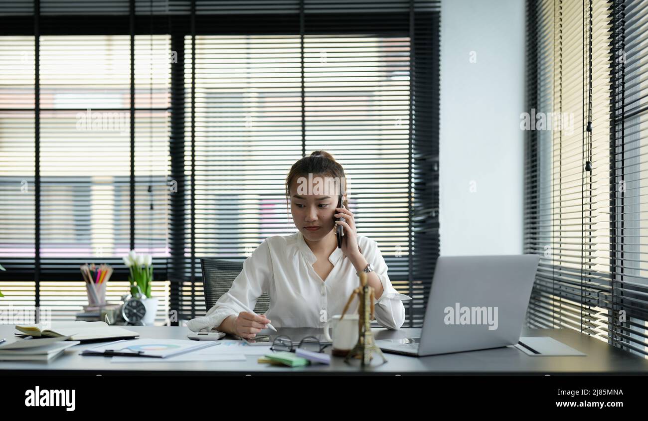 Portrait d'une femme d'affaires asiatique qui fait un appel téléphonique et sourit tout en travaillant au bureau informatique Banque D'Images