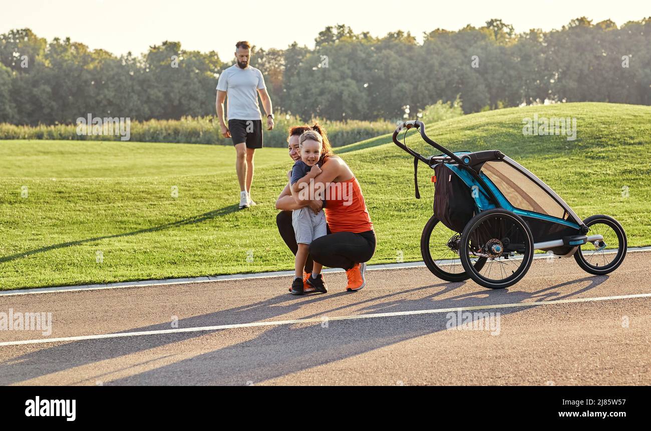 Une jeune famille heureuse avec son fils passe du temps ensemble tout en marchant avec une poussette dans le parc de la ville. Jour de la famille Banque D'Images