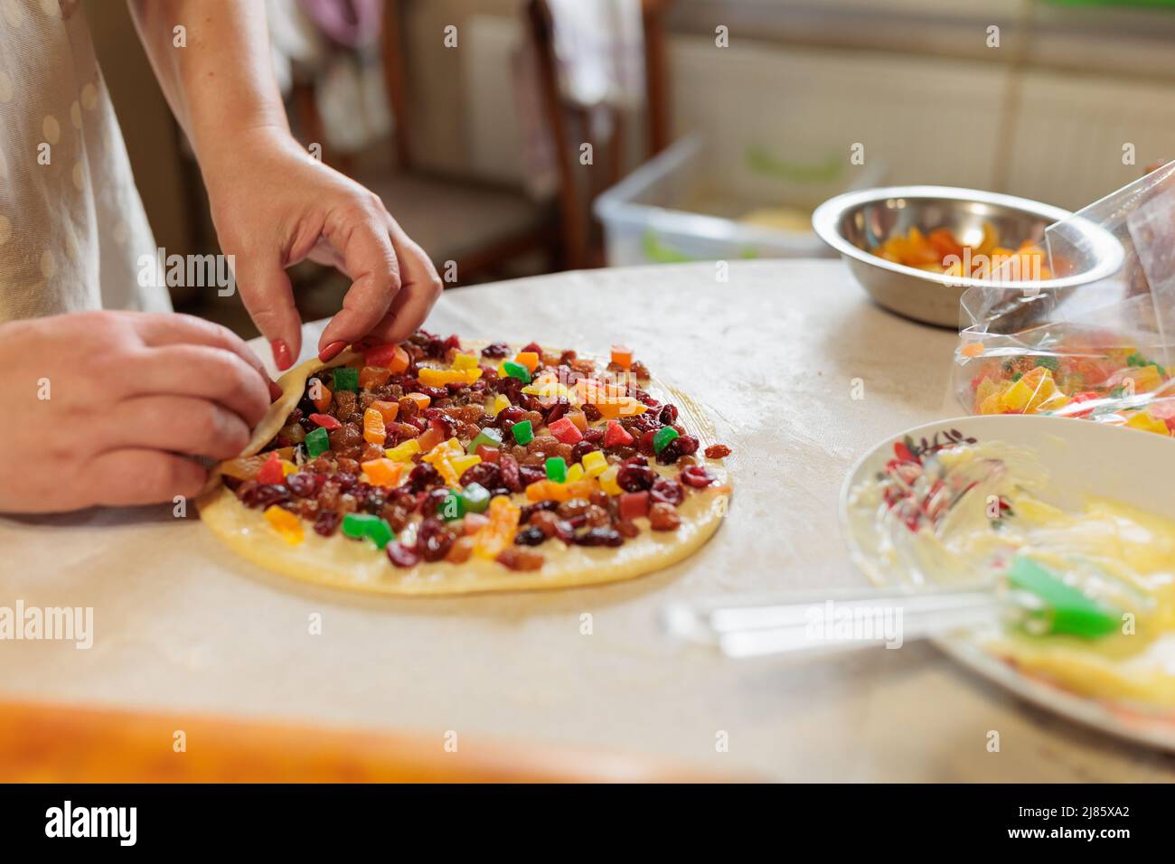 les mains des femmes tortillent la pâte avec des raisins secs et des fruits confits. pâte à gâteau crue pour kraffin Banque D'Images