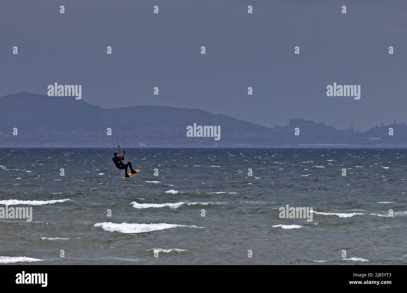 Longniddry, East Lothian, Écosse, Royaume-Uni. 13th mai 2022. Une scène monochromatique et un vent extrême pour ce kitesurfer solitaire habile avec son cerf-volant orange, Avec des vents de 43 km/h et des rafales potentielles de 74 km/h lui permettant de devenir roi du château en faisant de l'air au-dessus de la Firth of Forth avec le château d'Édimbourg et le centre-ville en arrière-plan. Crédit : Arch White/alamy Live News. Banque D'Images