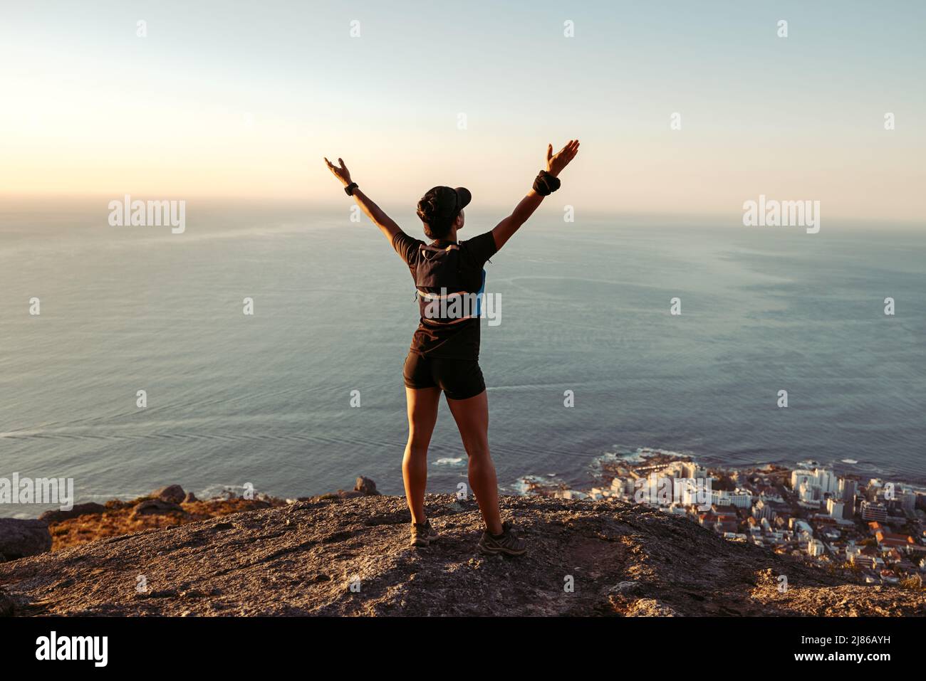 Vue arrière de la femme en forme debout sur le sommet de la montagne en regardant la vue avec les bras larges ouverts Banque D'Images