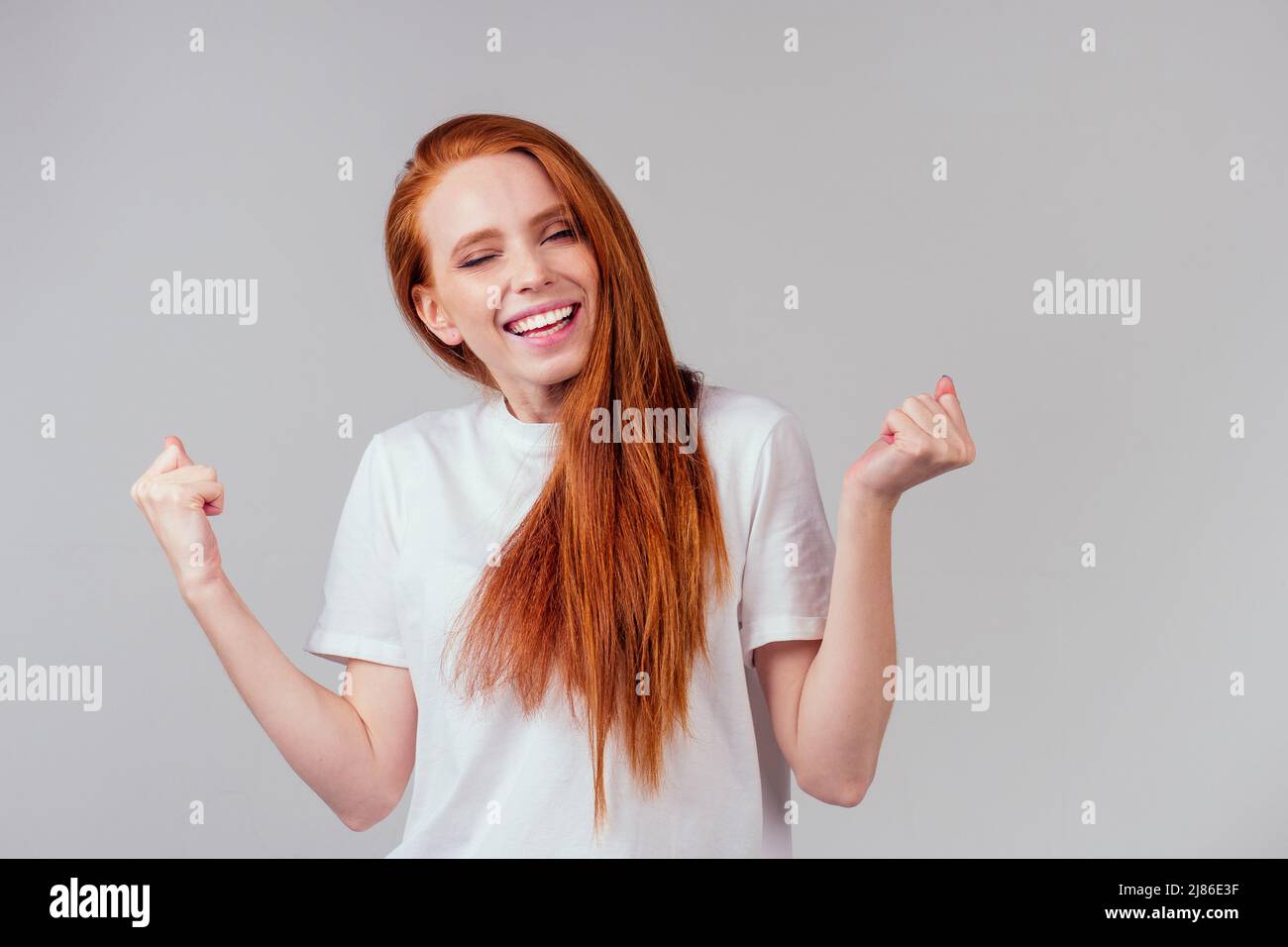 femme au gingembre rouge se sentant heureuse, portant un t-shirt en coton blanc sur fond gris de studio Banque D'Images