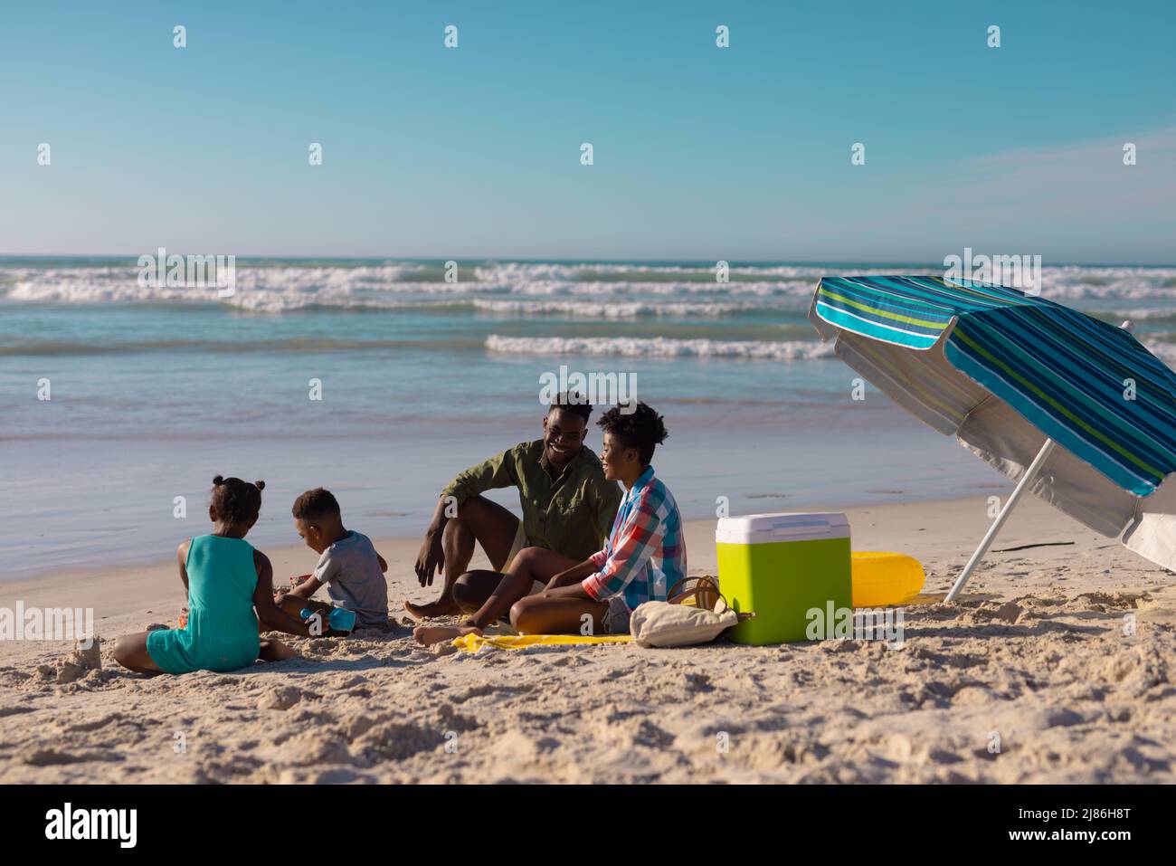 Jeunes parents afro-américains avec leur fils et leur fille appréciant à la plage contre le ciel bleu le jour ensoleillé Banque D'Images