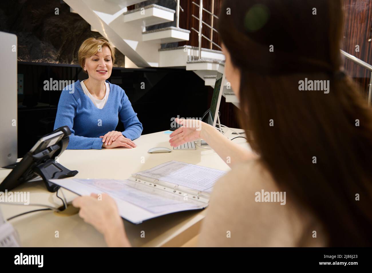 Charmante femme blonde de race blanche, consultante portant des vêtements décontractés conversant avec une cliente à la réception Banque D'Images