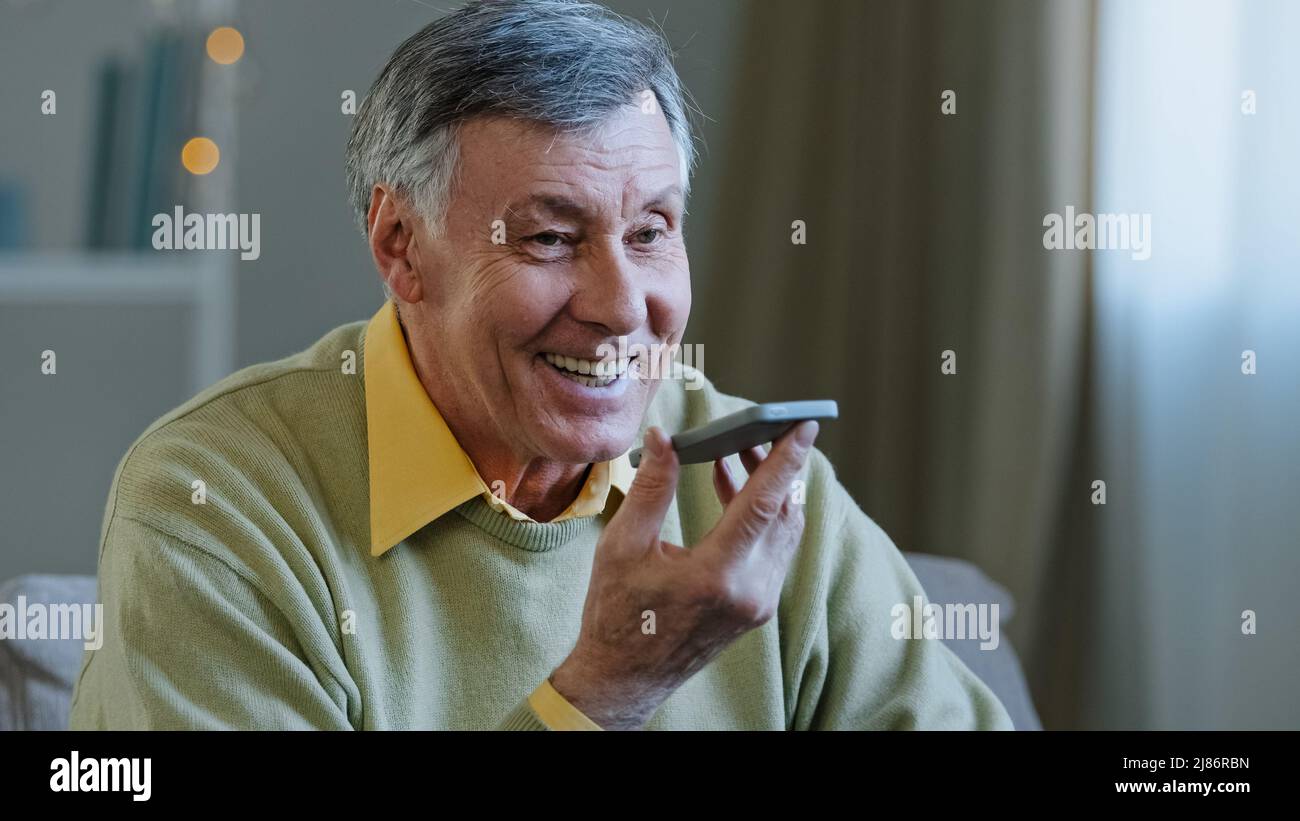 Mature gris-cheveux 60s homme 70s homme âgé à la maison tenir smartphone parler à voix haute au téléphone microphone haut-parleur message vocal à l'aide du haut-parleur Banque D'Images