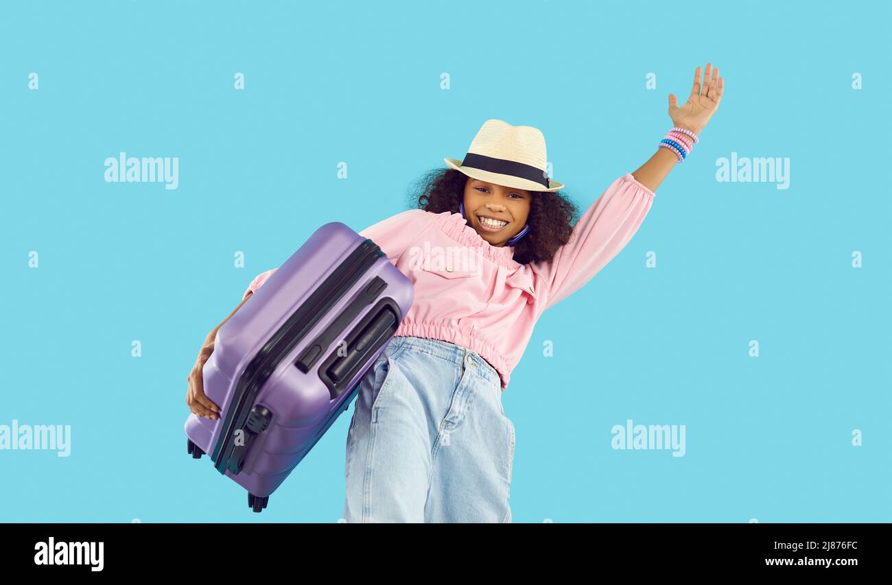 Joyeux enfant noir en vacances d'été, portant une valise, souriant et agitant la main Banque D'Images
