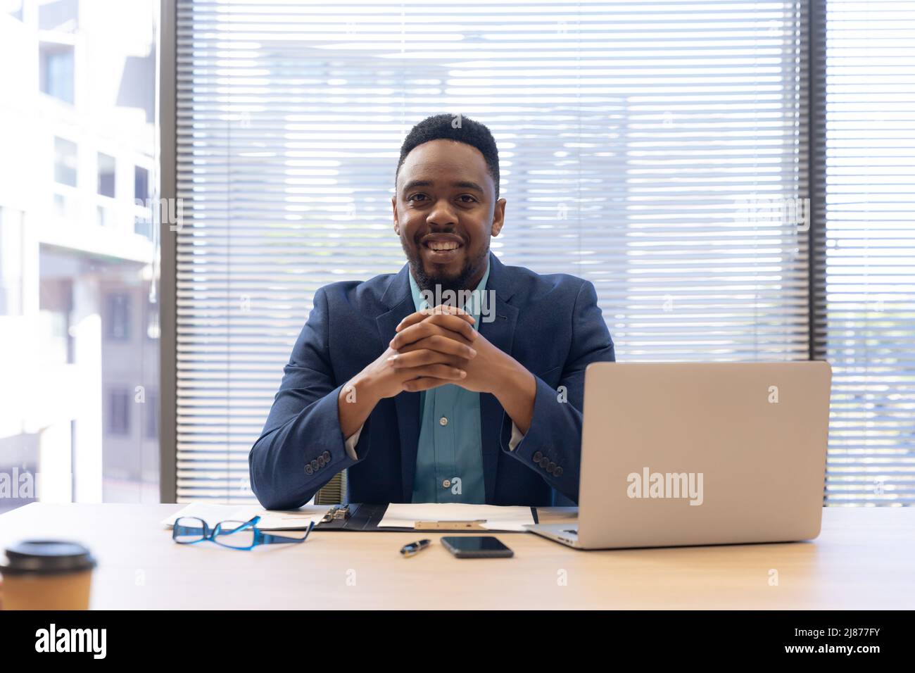 Portrait d'un homme d'affaires afro-américain souriant assis avec un ordinateur portable sur un lieu de travail moderne Banque D'Images