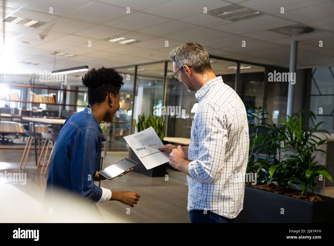 Des collègues biraciaux examinent le document tout en discutant ensemble lors d'une réunion sur un lieu de travail moderne Banque D'Images