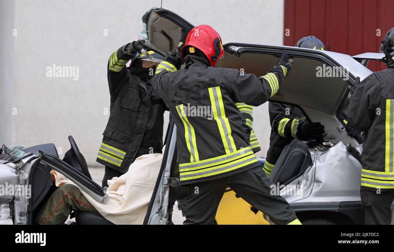 après l'accident de la route, les pompiers retirent le capot de la voiture pour libérer la personne blessée des tôles tordues du véhicule accidenté Banque D'Images