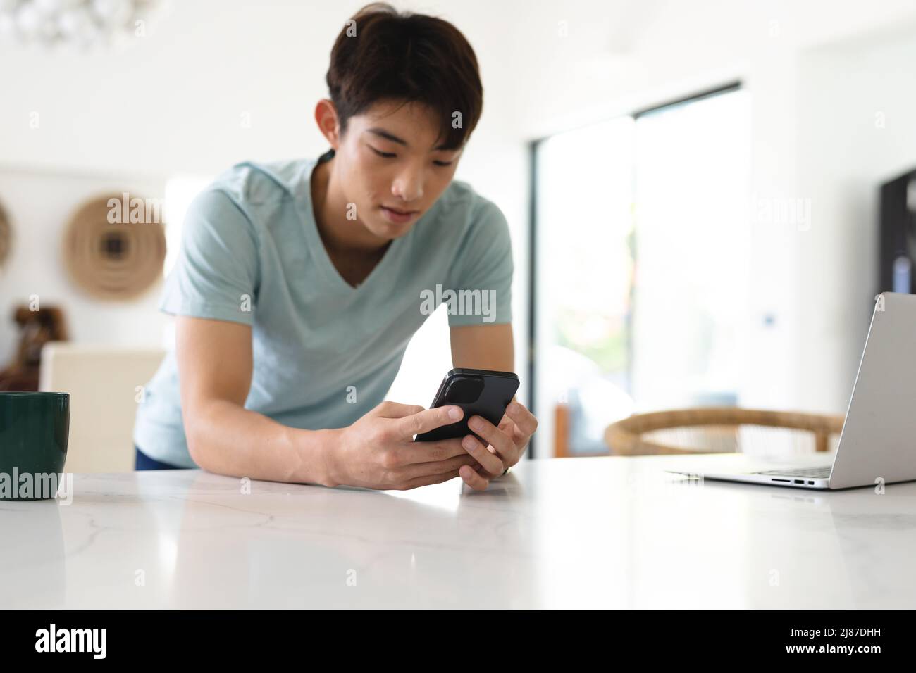 Adolescent asiatique sérieux portant un t-shirt bleu avec un ordinateur portable sur une table utilisant un téléphone mobile, espace de copie Banque D'Images