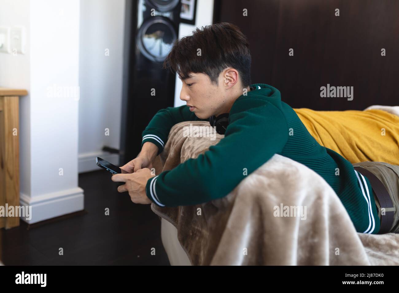 Vue latérale d'un adolescent d'asie à l'aide d'un smartphone tout en étant allongé sur le canapé dans le salon Banque D'Images