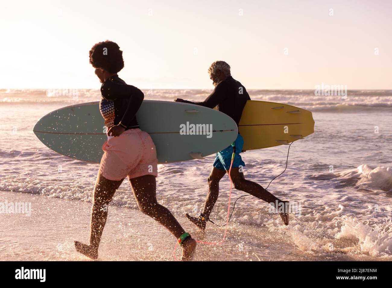 Couple afro-américain joyeux avec planches de surf en mer contre ciel clair au coucher du soleil Banque D'Images