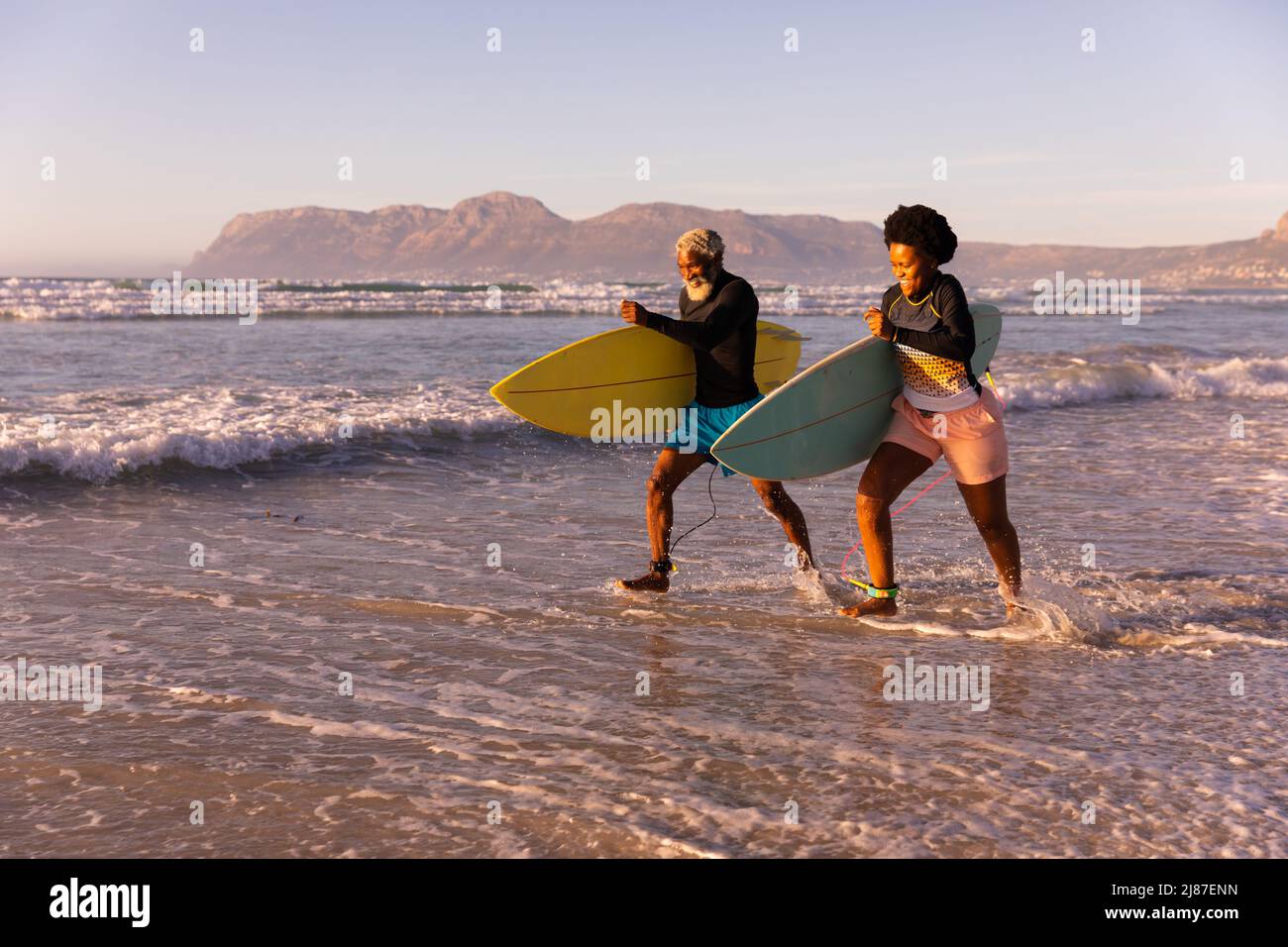 Couple afro-américain espiègle avec planches de surf en mer contre ciel clair au coucher du soleil Banque D'Images