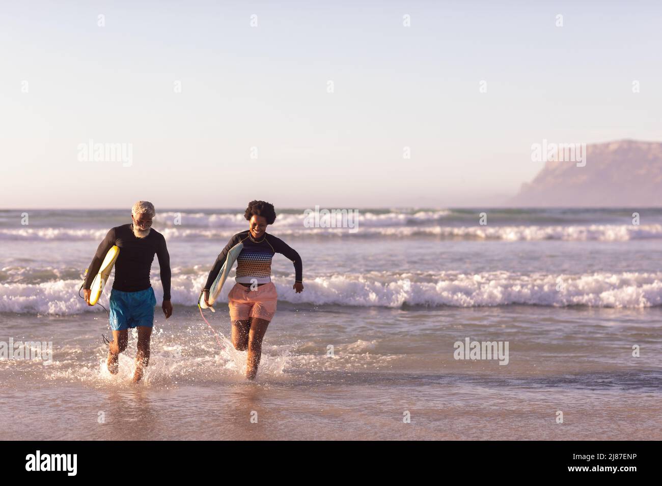 Couple afro-américain insouciant avec planches de surf au milieu de vagues contre ciel clair, espace de copie Banque D'Images