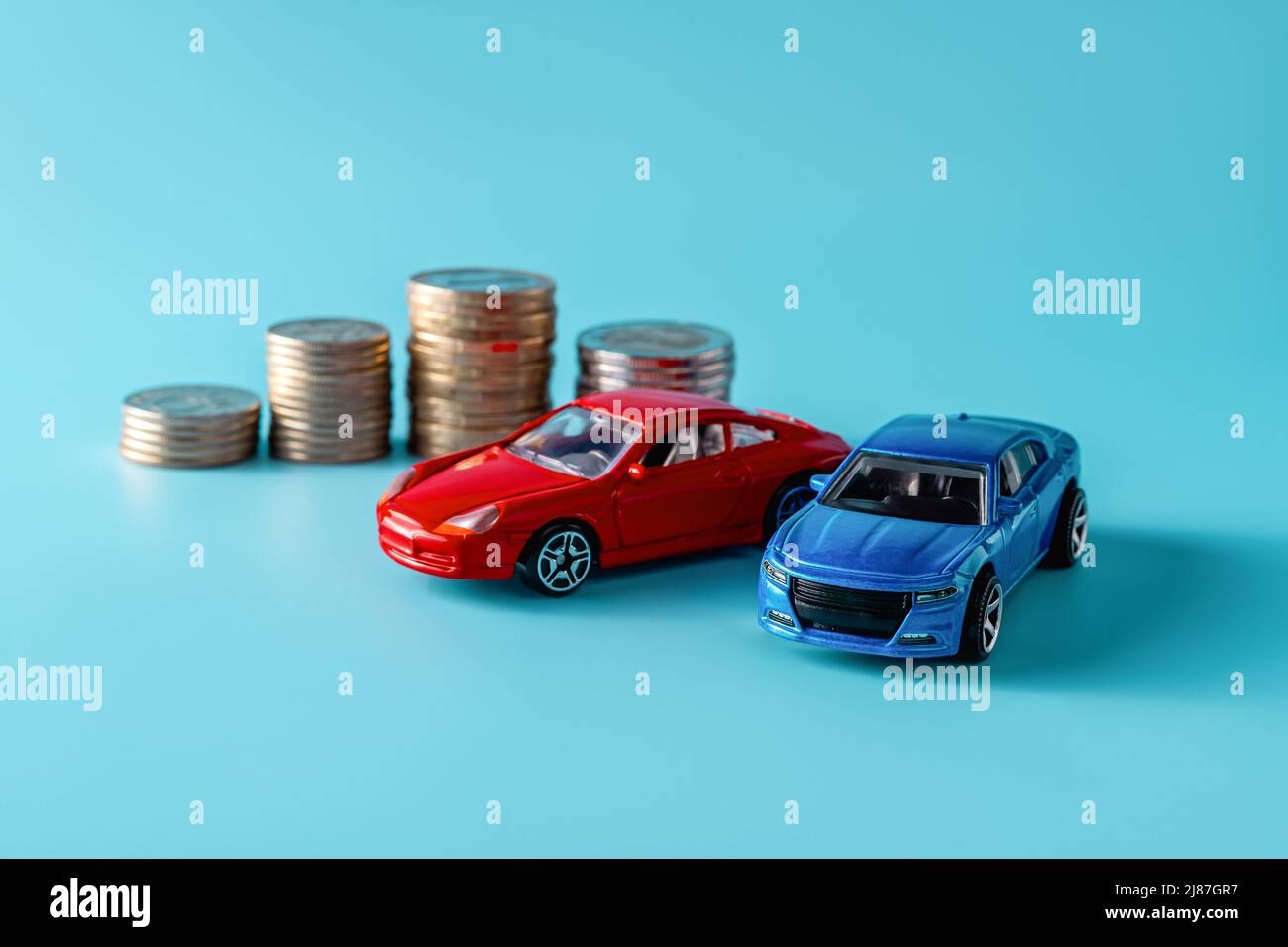 Varna, Bulgarie, 10 mai 2022. Modèles de voitures miniatures rouges et bleues à des piles de pièces sur fond bleu. Prêt auto, assurance, économiser de l'argent pour une voiture Banque D'Images