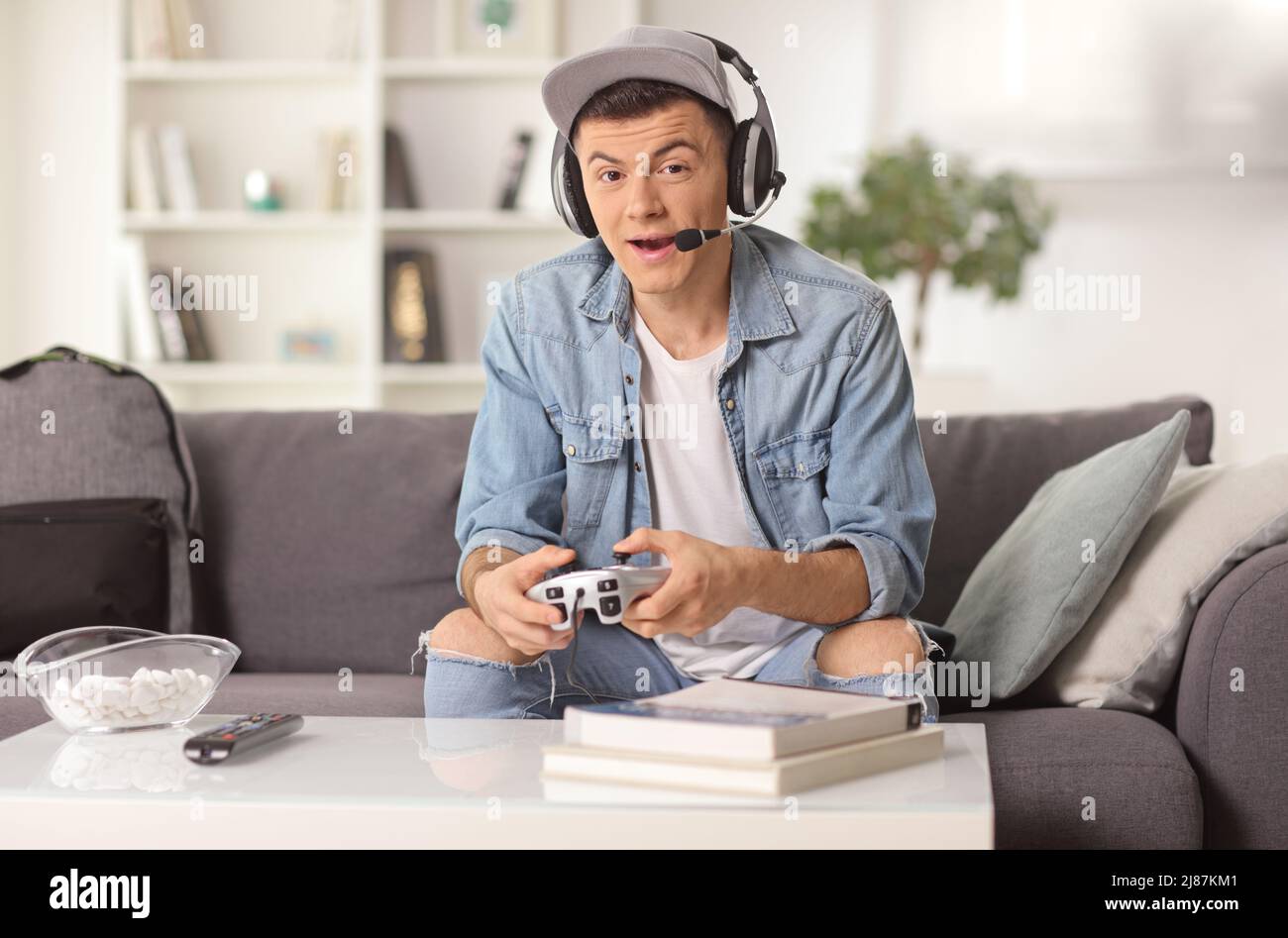 Un gars avec un casque et un joystick assis sur un canapé et jouant à des jeux vidéo à la maison Banque D'Images