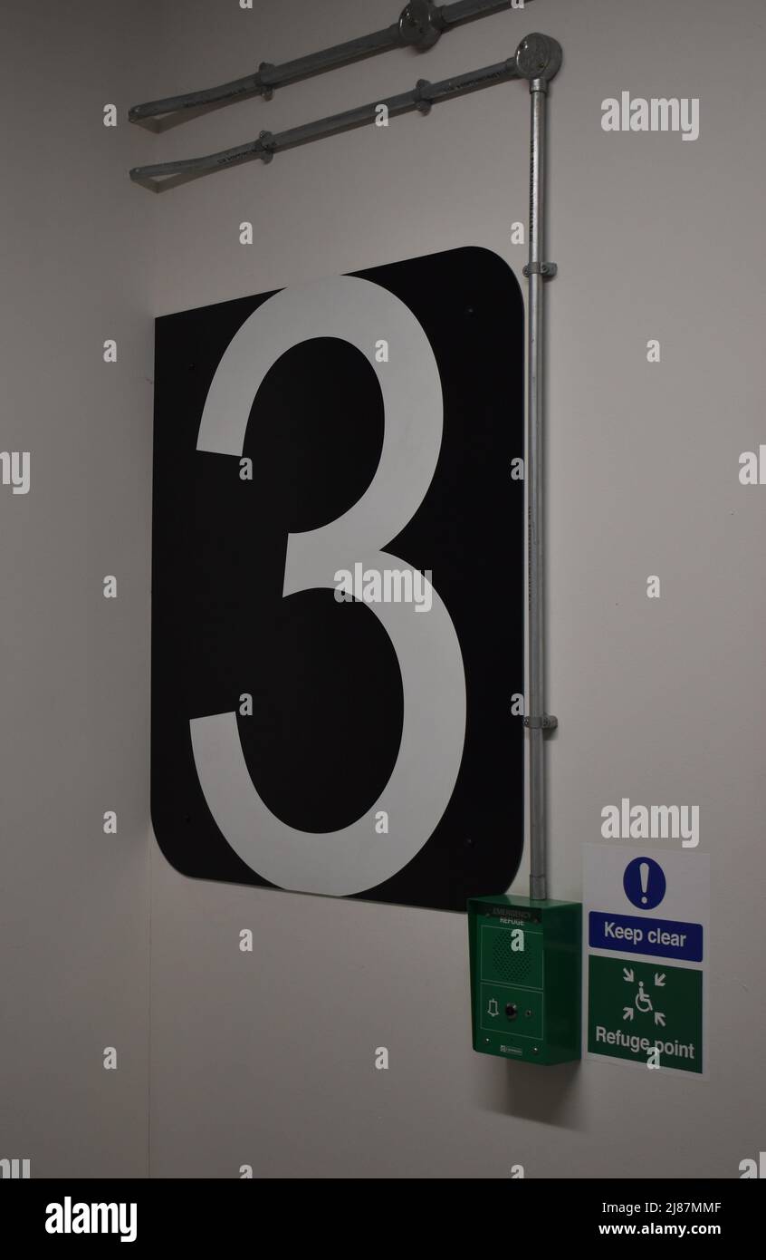 Un chiffre blanc « 3 » sur fond noir dans un parking à plusieurs étages. Banque D'Images