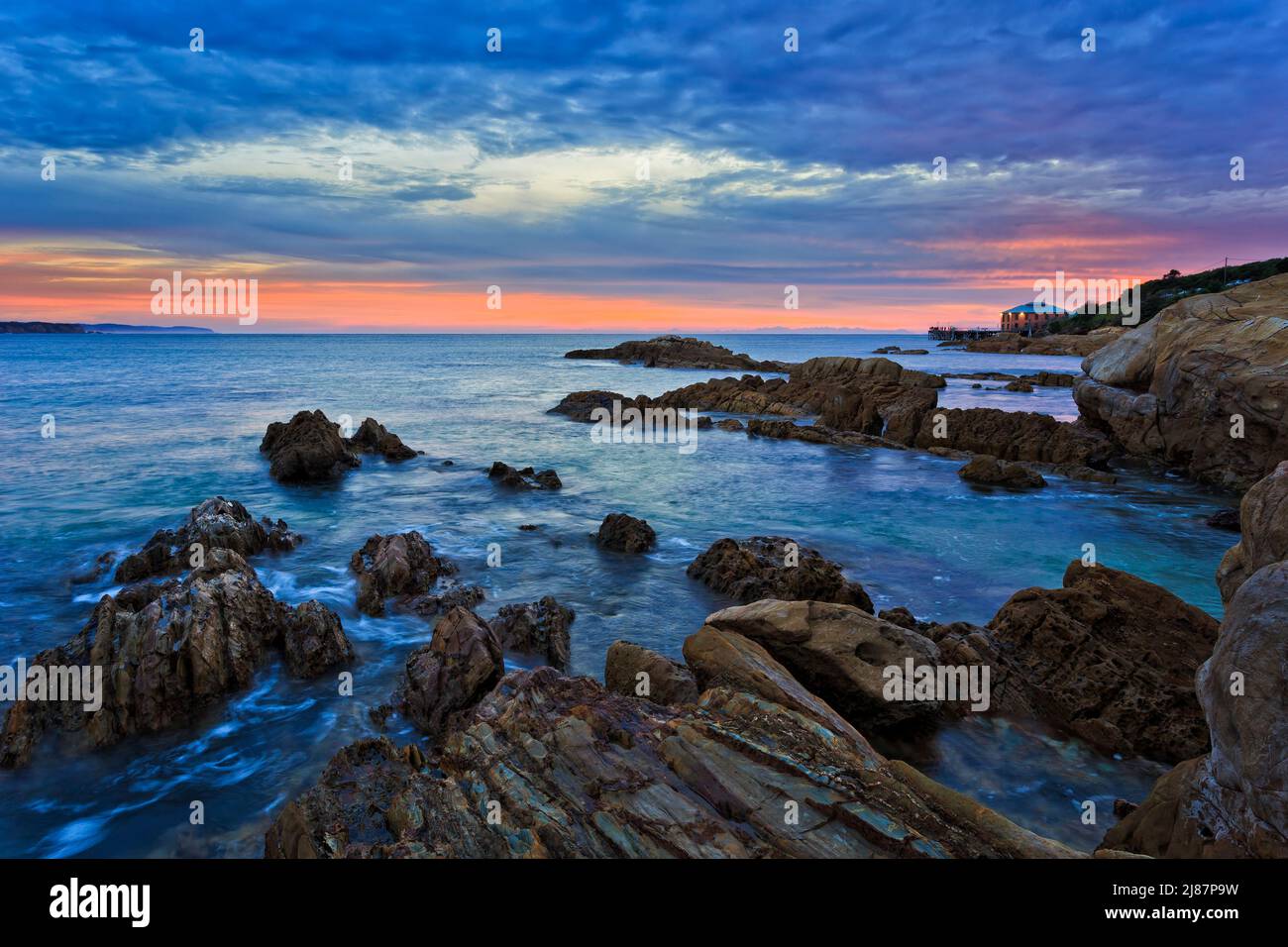 Rochers en grès submergés de la plage de Tathra sur la côte de Sapphire en Australie, au lever du soleil pittoresque. Banque D'Images