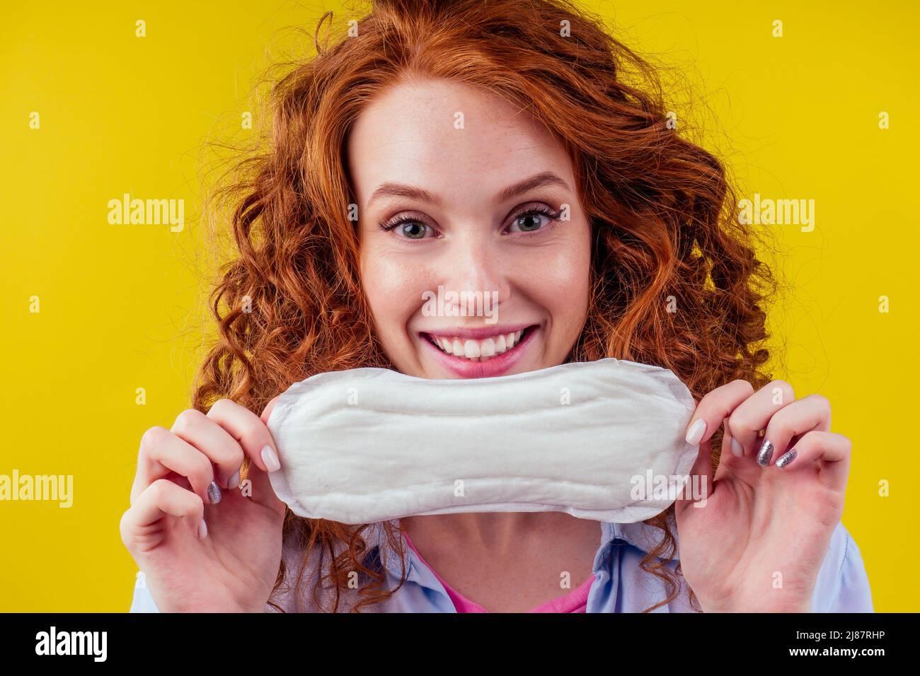 Gros plan photo d'une jeune femme d'affaires à tête rouge, bouclés et gingembre en chemise bleue tenant un tampon d'hygiène en choisissant un fond jaune de studio de tampon Banque D'Images