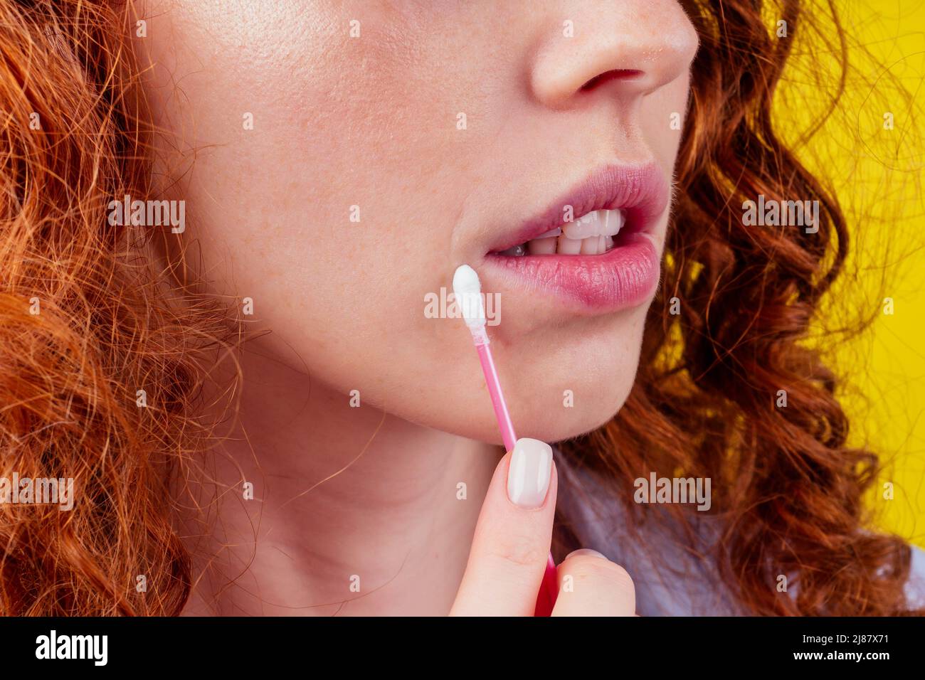caucasien belle redhaired curly femelle utilisation coton bâton, test de sonde biométrique d'adn dans le fond jaune studio Banque D'Images