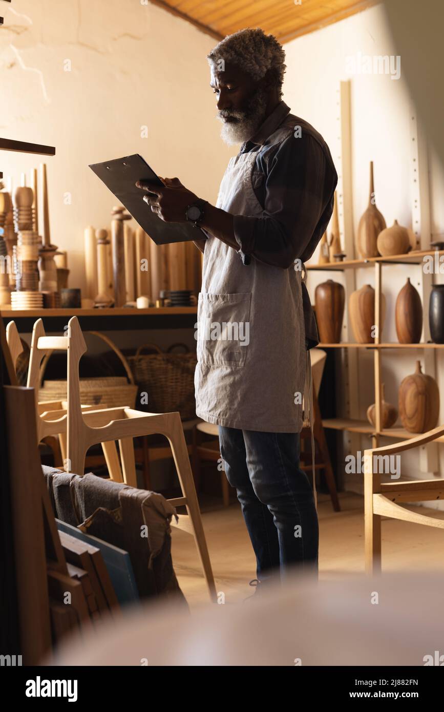 Menuisier afro-américain mature écrivant dans le presse-papiers tout en travaillant dans l'atelier Banque D'Images