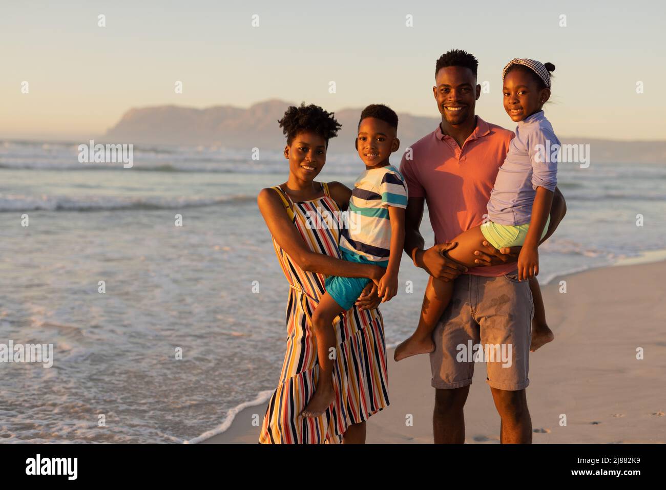 Portrait de parents afro-américains souriants portant leur fils et leur fille debout contre la mer Banque D'Images