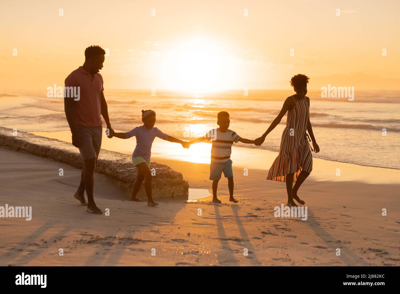 Jeunes parents afro-américains tenant les mains de leur fille et de leur fils tout en marchant à la plage contre le ciel Banque D'Images