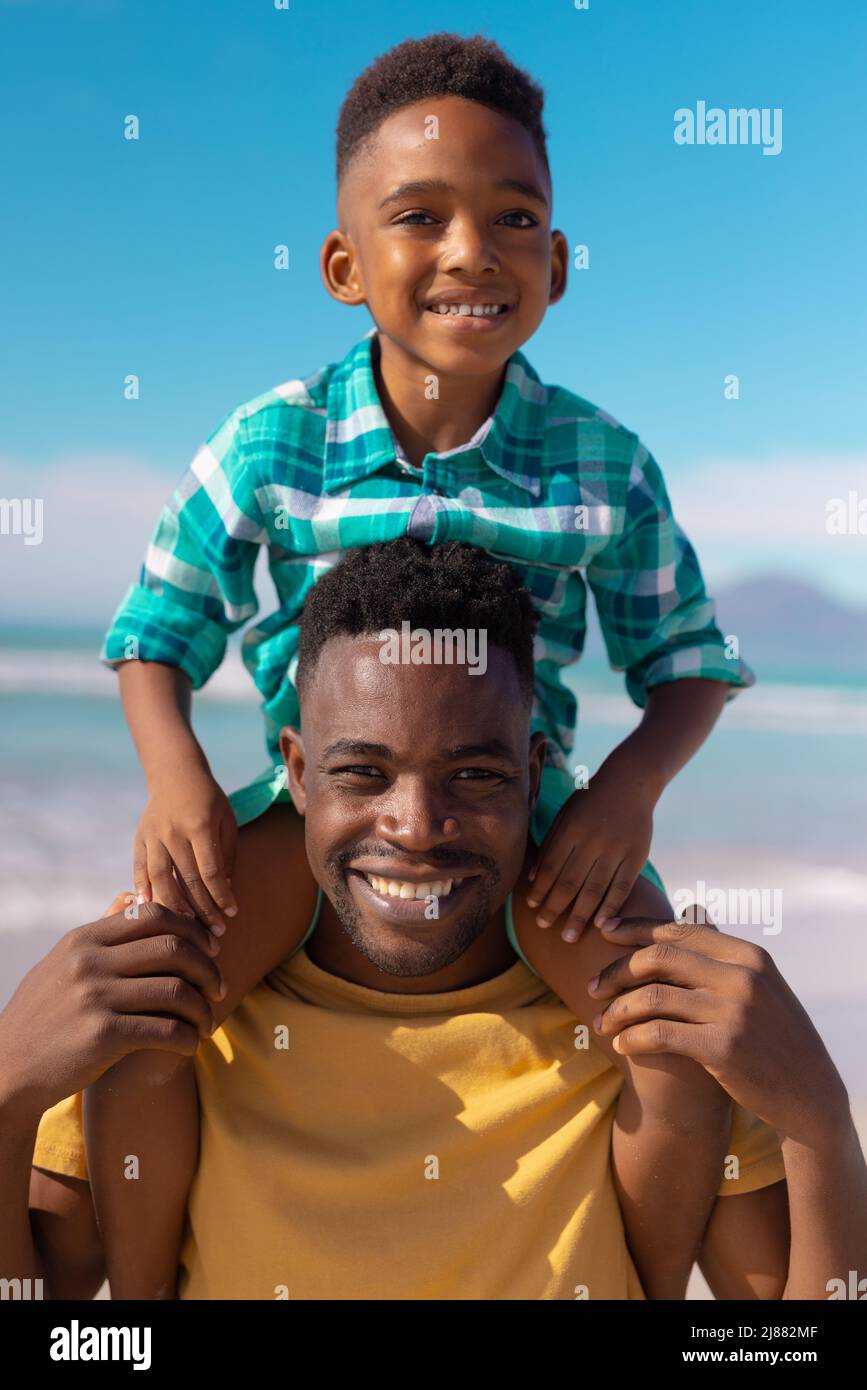 Portrait d'un jeune homme afro-américain souriant portant un fils mignon sur les épaules contre le ciel bleu Banque D'Images