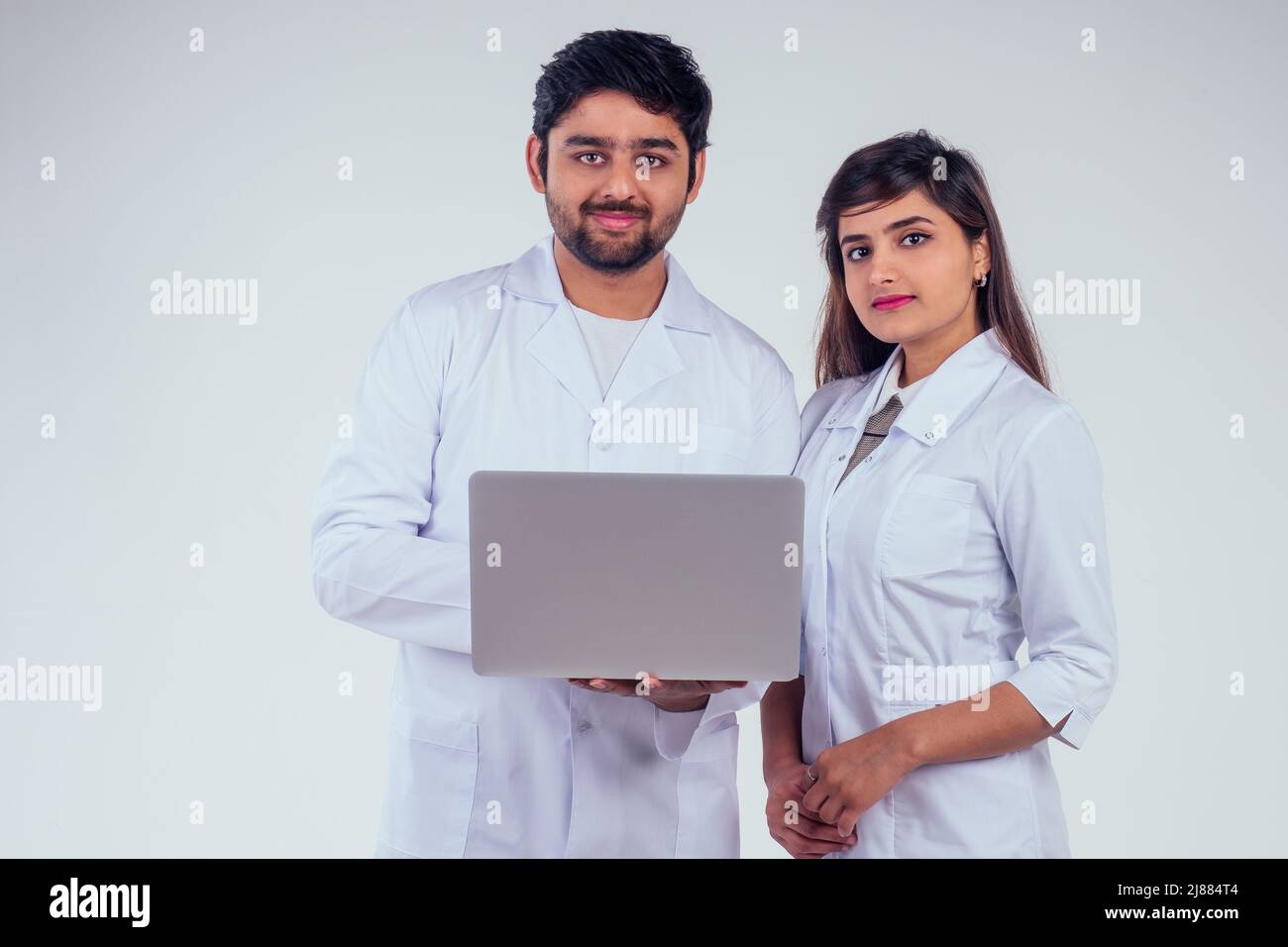 belle femme indienne et beau dinde homme portant un blazer blanc portant un ordinateur portable et regardant l'appareil photo en arrière-plan studio Banque D'Images