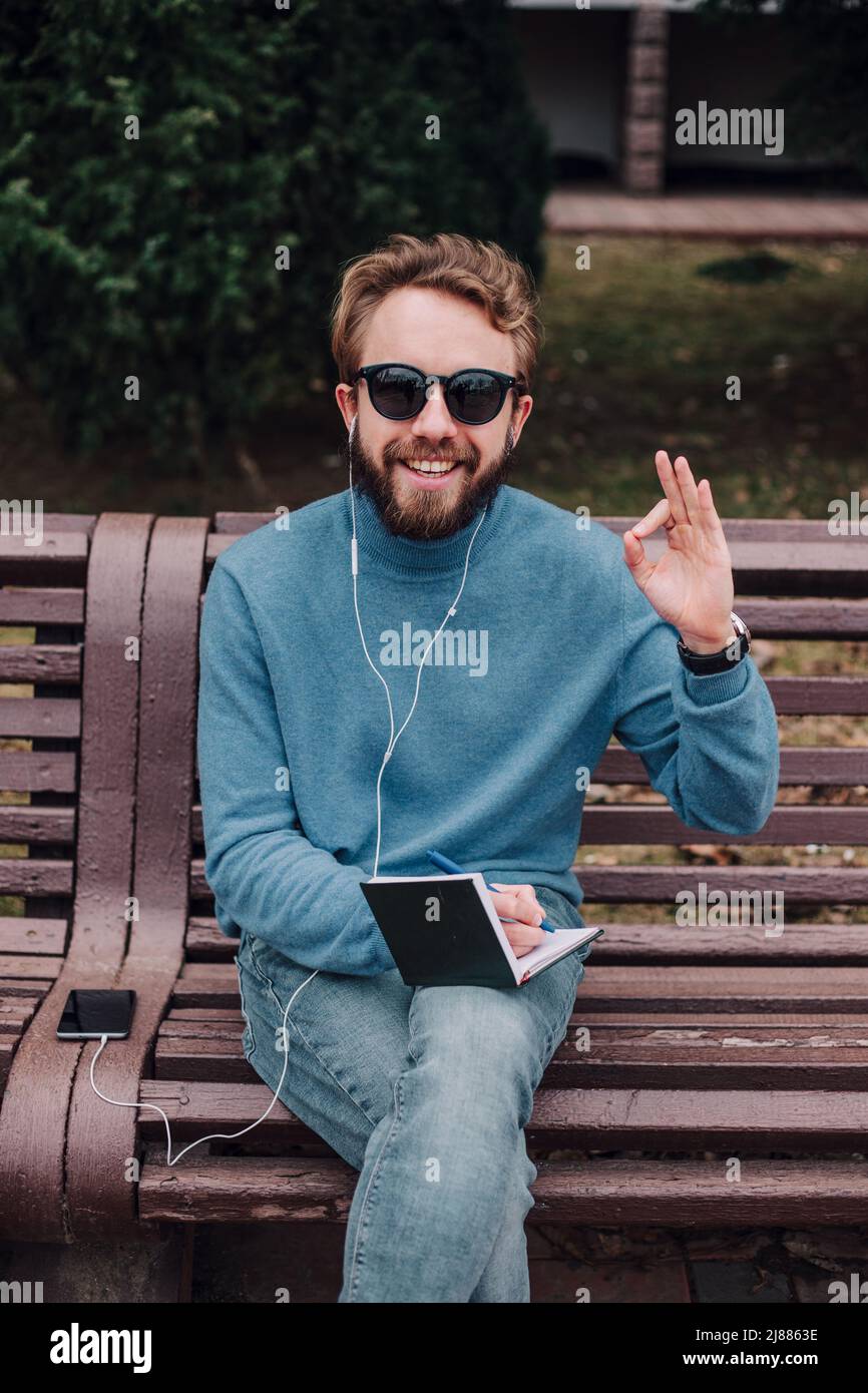 jeune gay hipster garçon avis des idées siting dans un parc et écouter de la musique par des écouteurs Banque D'Images