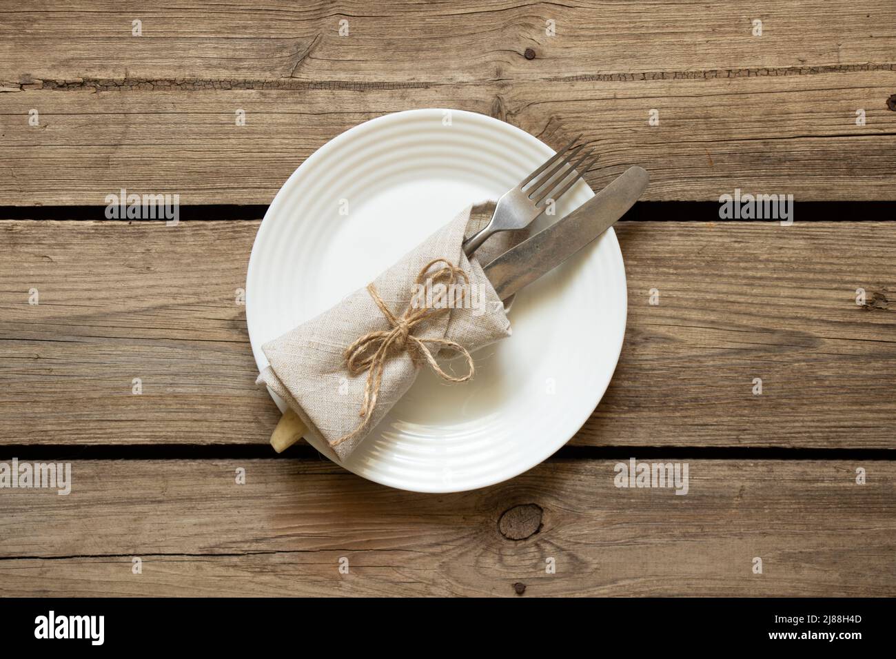 Une assiette blanche et une fourchette avec un couteau se trouvent sur une ancienne table en bois dans la cuisine à la maison, affaires de restaurant, appareils de cuisine Banque D'Images