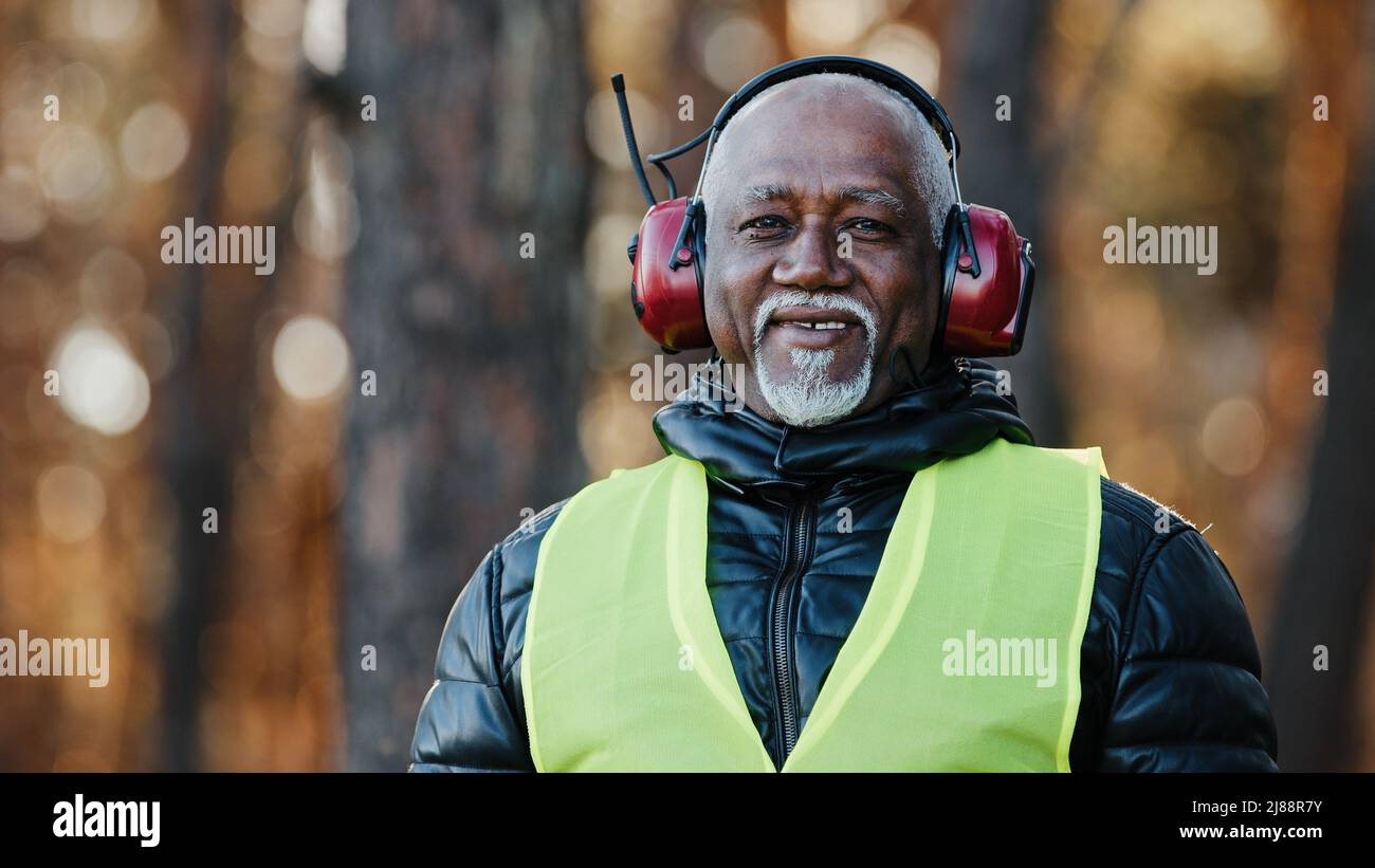 Homme âgé ingénieur forestier professionnel en casque de protection insonorisé debout dans la forêt regardant la caméra contremaître afro-américain mature Banque D'Images