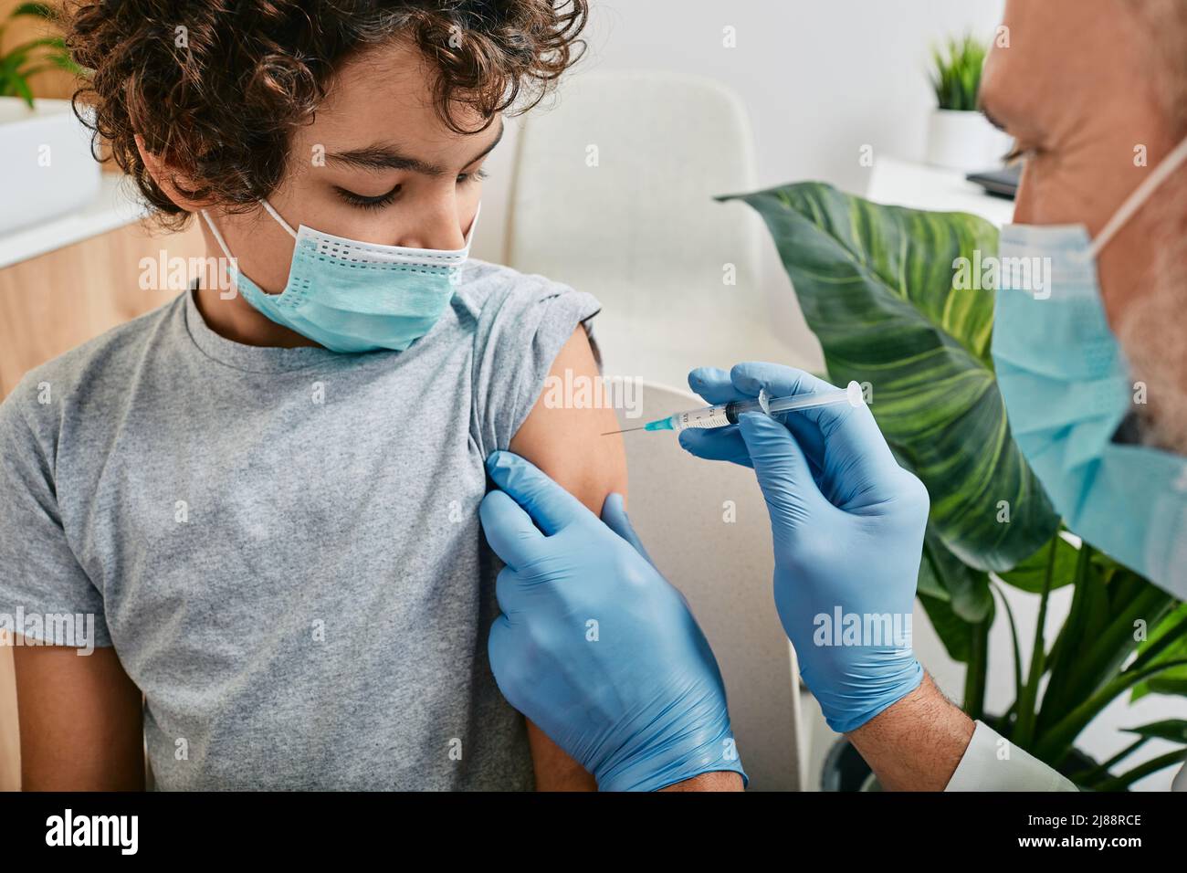Vaccinations de routine pour un enfant. Adolescent portant un masque médical lorsqu'il est vacciné par un pédiatre mature à la clinique médicale Banque D'Images
