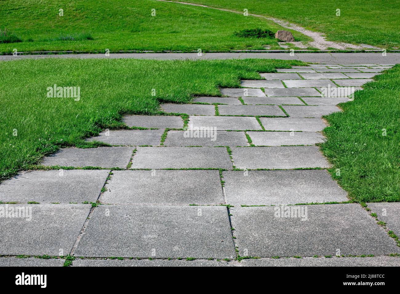 sentier de parc constitué de carreaux carrés cultivés avec de l'herbe dans un parc avec une pelouse verte en gros plan sur le parc avec prairie et route asphaltée éclairée par su Banque D'Images