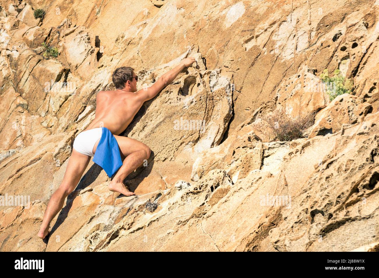 Jeune homme athlétique escalade libre sans équipement sur une pente de roche dangereuse - concept aventureux de liberté et de contact avec la nature sauvage Banque D'Images