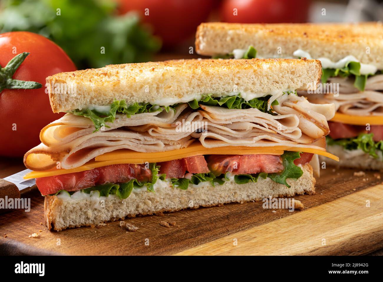 Gros plan du sandwich à la dinde tranchée, au fromage, à la laitue et à la tomate sur du pain grillé coupé en deux sur une planche à découper Banque D'Images