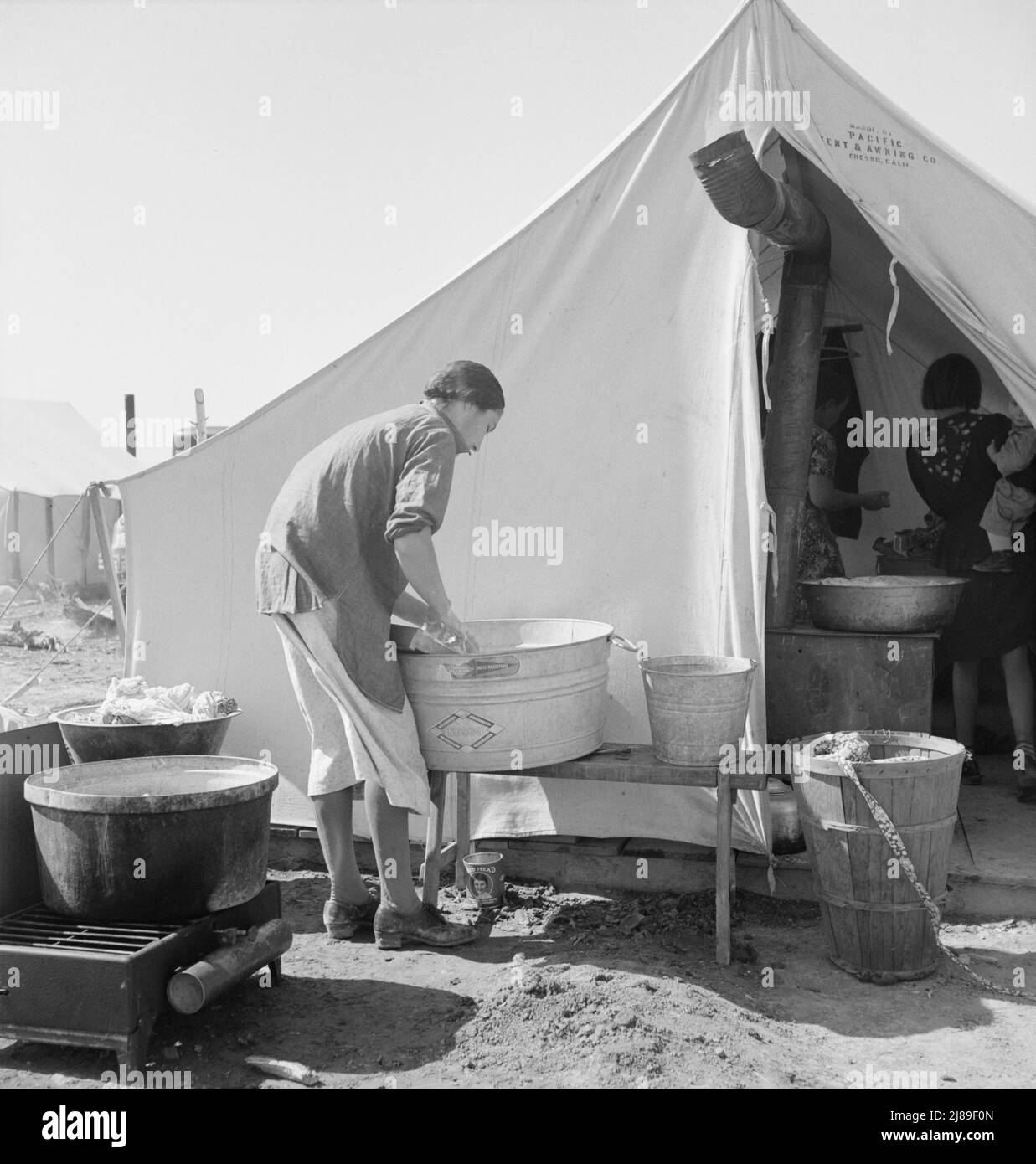 Camp de préparateur de pois. Cette famille était propriétaire d'une ferme en Oklahoma, a perdu sa ferme et depuis trois ans, « nos enfants ont été draggin » autour de la Californie. Nous sommes un cas d'espèce. » Calipatria, Imperial Valley, Californie. [Femme utilisant un bain de toilette résistant à la rouille en acier Nesco]. Banque D'Images