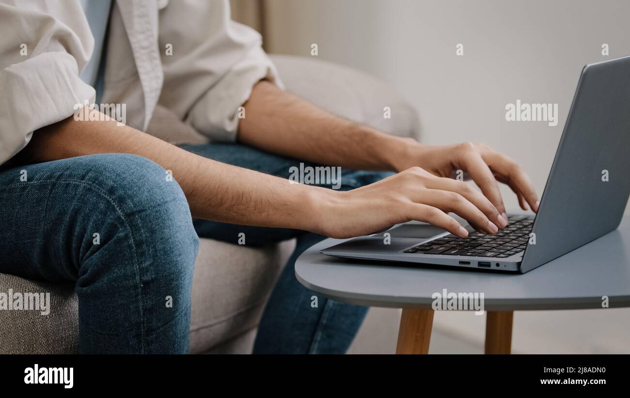 Gros plan des mains de sexe masculin sur le clavier de l'ordinateur portable. Homme inconnu homme d'affaires inconnu en Jean chemise décontractée assise sur un canapé avec ordinateur de travail Banque D'Images