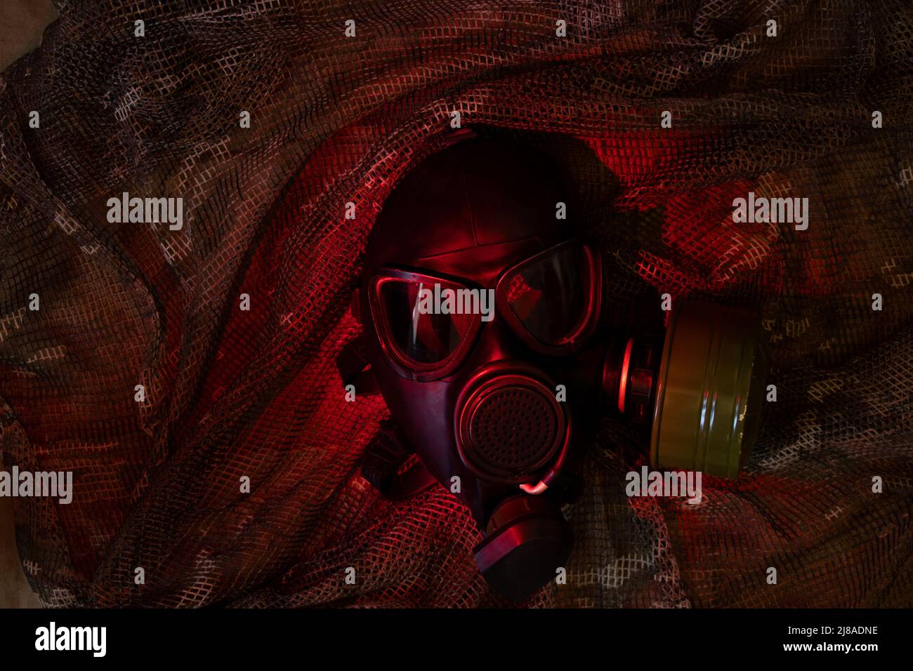 Masque à gaz noir repose sur un costume militaire de camouflage avec éclairage rouge, attaque au gaz, équipement militaire, risque chimique Banque D'Images